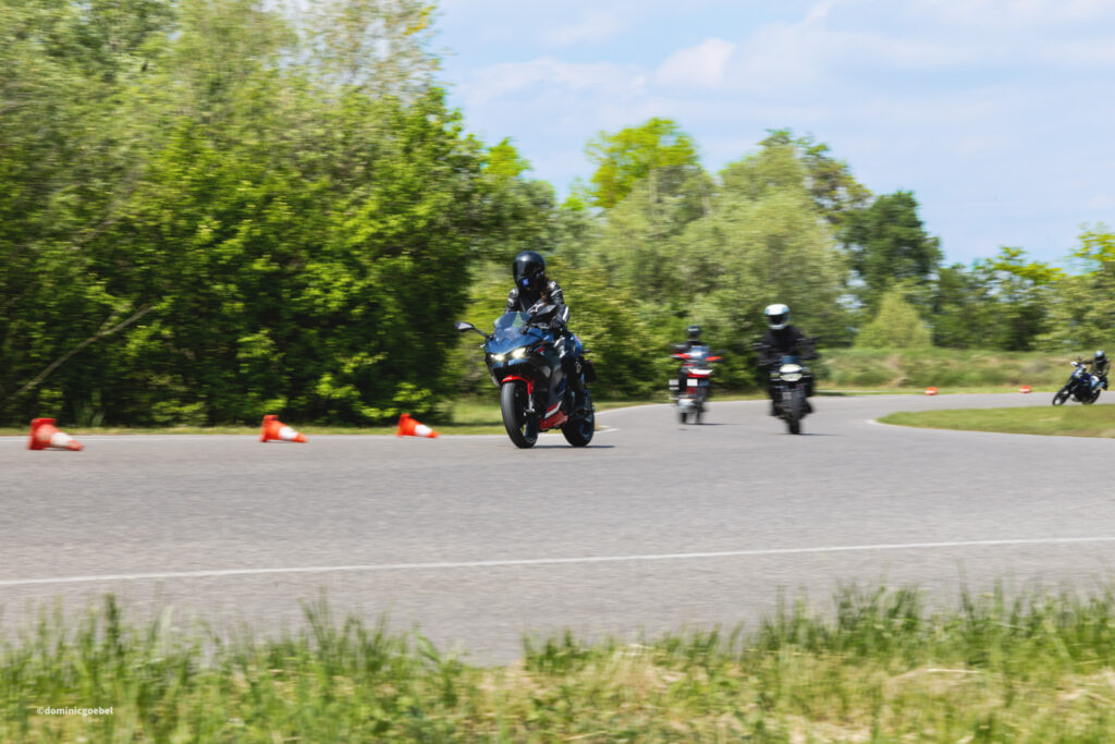 Motorrad Testtage 2026 Teesdorf c Dominic Goebel-13 - I love my moped Motorcyclists riding a curved road with orange traffic cones and green trees in the background on a sunny day.