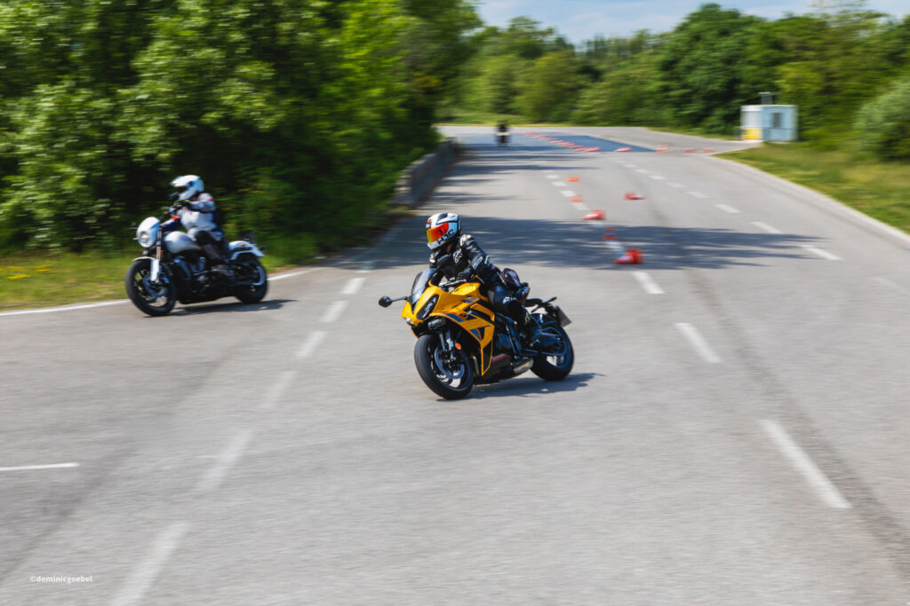Motorrad Testtage 2026 Teesdorf c Dominic Goebel-18 - I love my moped Motorcyclists ride along a cone-marked road course on a sunny day, with a yellow sport bike leading the way and a rider in protective gear nearby.