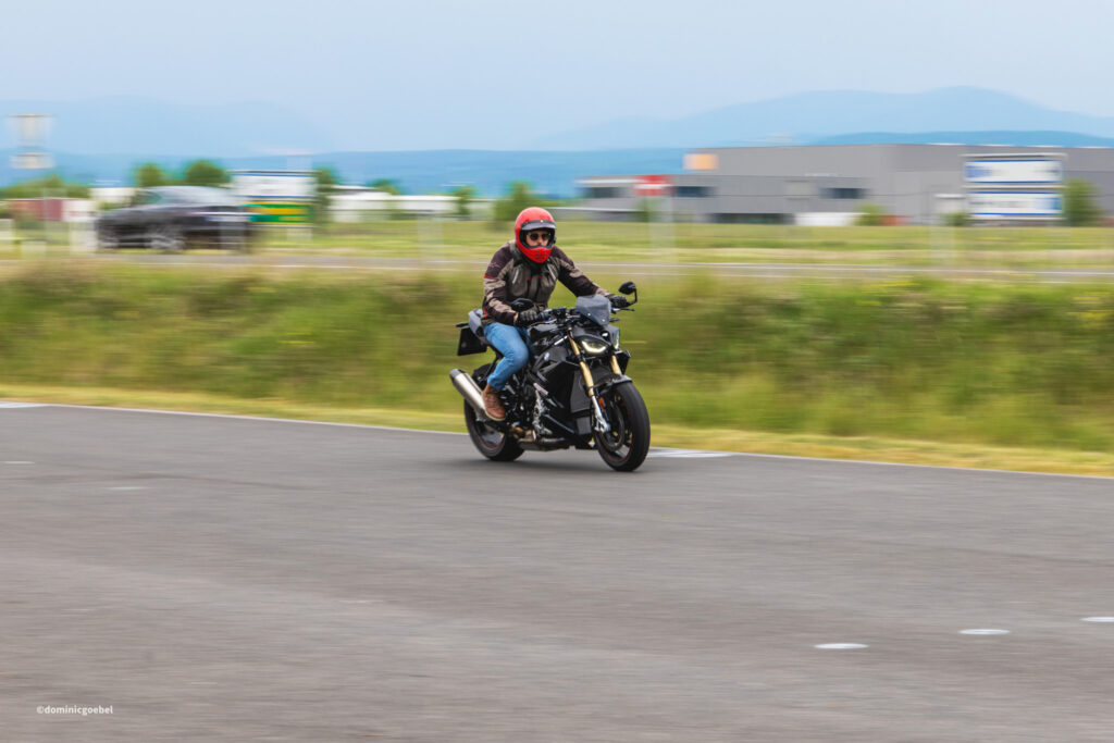 Motorrad Testtage 2026 Teesdorf c Dominic Goebel-28 - I love my moped Motorcyclist wearing a red helmet rides a black motorcycle on a blurred road background. (informative)