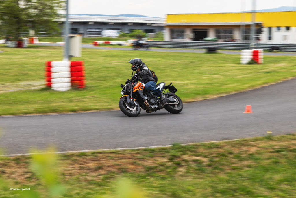 Motorrad Testtage 2026 Teesdorf c Dominic Goebel-30 - I love my moped Motorcycle racer in black gear leaning into a turn on a racetrack with orange bike, blurred background and red-white barriers nearby.