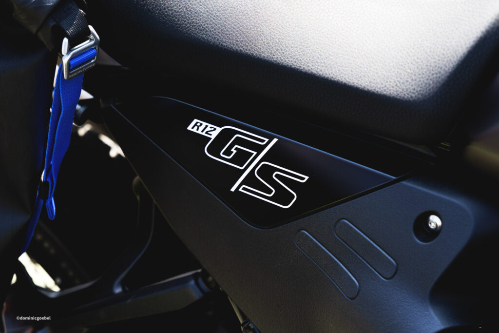 Motorrad Testtage 2026 Teesdorf c Dominic Goebel-38 - I love my moped Close-up of a black motorcycle seat area with a white R12 graphic sticker and a blue strap nearby in a glossy finish setting.