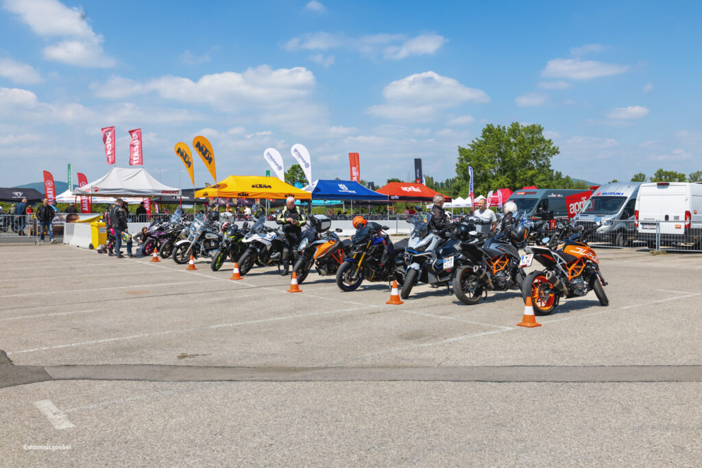 Motorrad Testtage 2026 Teesdorf c Dominic Goebel-9 - I love my moped Row of motorcycles parked at an outdoor motorcycle expo under a bright blue sky with tents and banners.