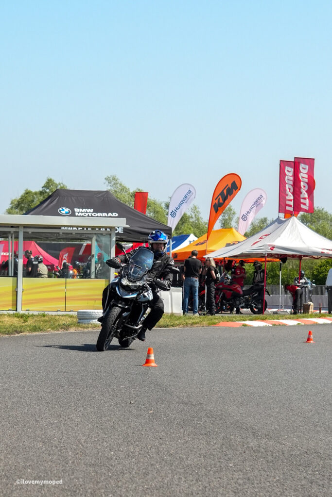 arge2rad-motorradtesttage2026-teesdorf-02 - I love my moped Motorcyclist on a sport bike navigates orange cones at an outdoor bike event with sponsor tents in the background.