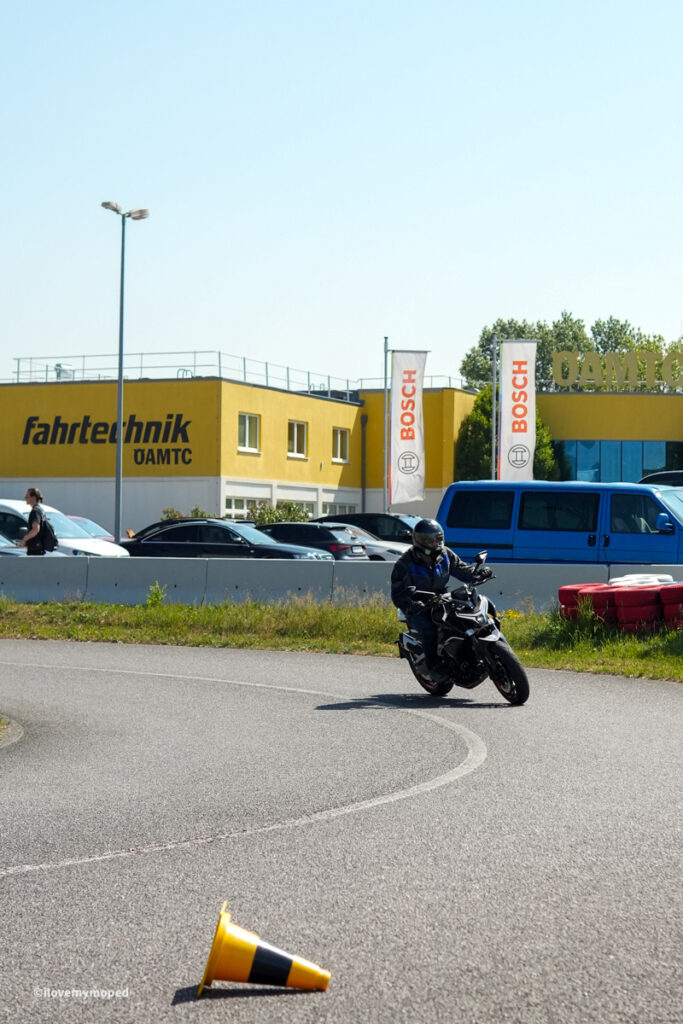 arge2rad-motorradtesttage2026-teesdorf-07 - I love my moped Motorcyclist wearing protective gear leans into a turn on a track beside a yellow building with Bosch flags.