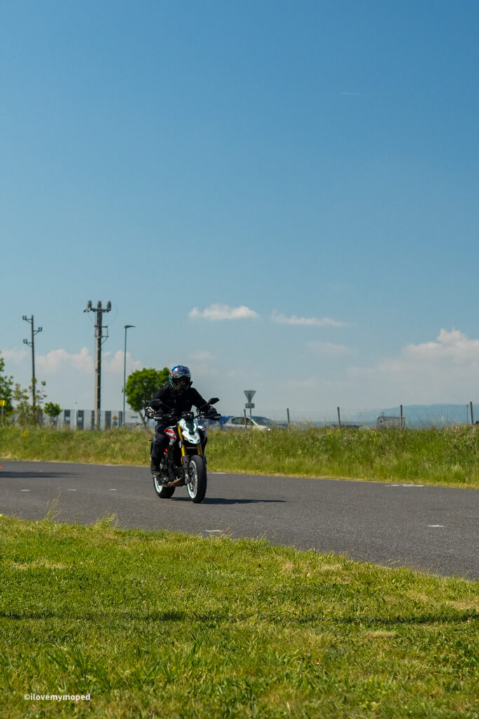 arge2rad-motorradtesttage2026-teesdorf-10 - I love my moped Motorcyclist wearing a helmet rides a motorcycle on a wide rural road under a blue sky.