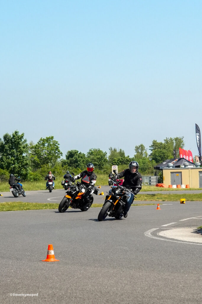 arge2rad-motorradtesttage2026-teesdorf-11 - I love my moped Motorcyclists navigate a cone-filled course on a sunny day, leaning into turns with helmets on.