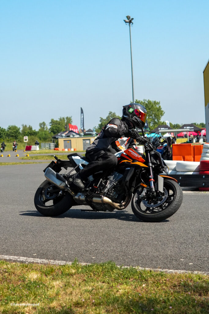 arge2rad-motorradtesttage2026-teesdorf-12 - I love my moped Motorcycle rider in full protective gear leaned into a left-hand turn on a racetrack, orange bike slicing through asphalt.