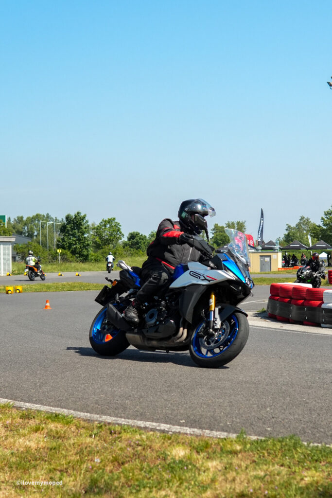arge2rad-motorradtesttage2026-teesdorf-13 - I love my moped Rider in black and red protective gear leaning into a turn on a blue-and-white sportbike on a paved track with orange cones in the foreground.