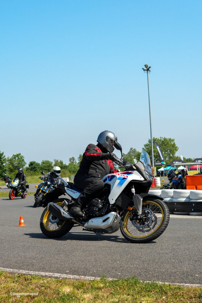 arge2rad-motorradtesttage2026-teesdorf-15 - I love my moped Rider in red-and-black gear leaning into a turn on a white Honda motorcycle with yellow rims at a closed-track course, cones in the foreground.