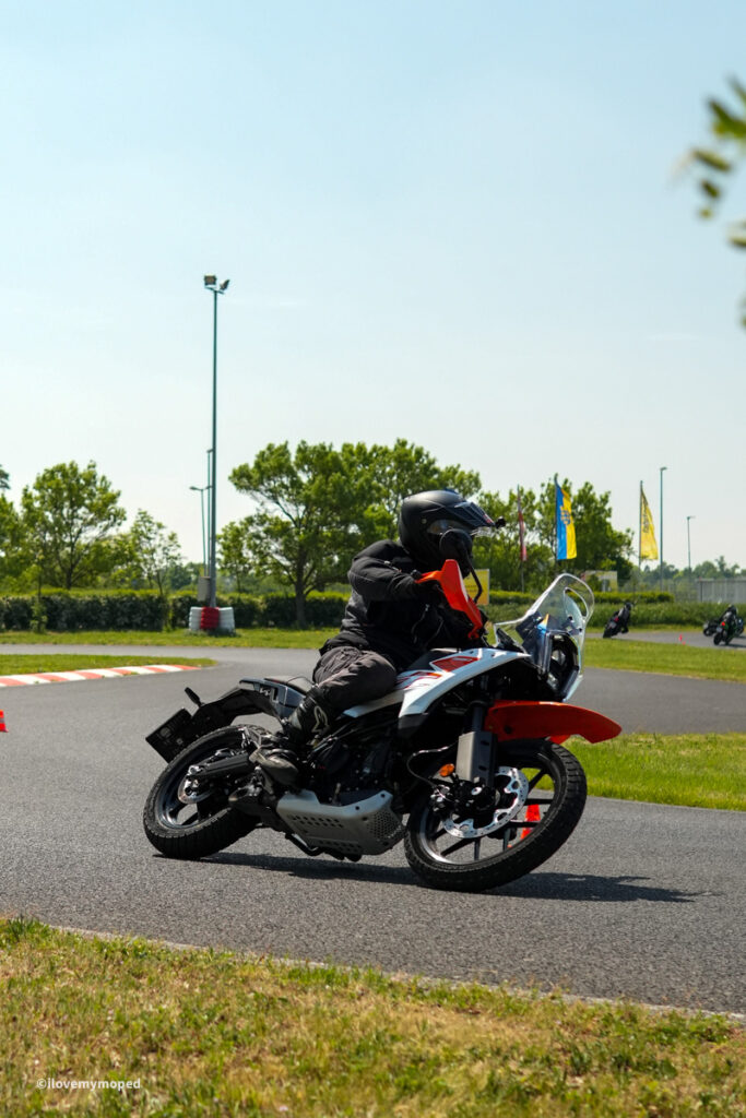 arge2rad-motorradtesttage2026-teesdorf-20 - I love my moped Motorcyclist in black gear leaning into a turn on a red-and-white adventure bike on a paved track.