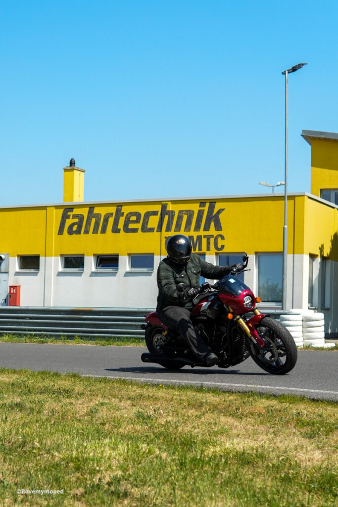arge2rad-motorradtesttage2026-teesdorf-24 - I love my moped Motorcyclist in protective gear leaning into a turn on a red sport bike on a race track with a yellow building reading 'fahrtechnik MTC' in the background