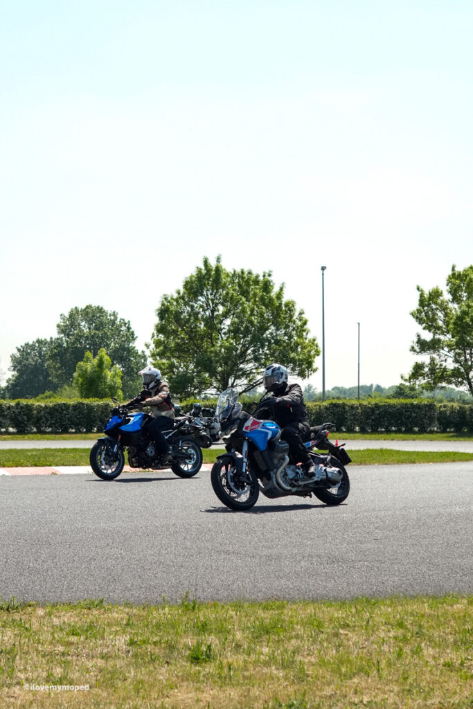 arge2rad-motorradtesttage2026-teesdorf-39 - I love my moped Two motorcyclists in protective gear riding blue motorcycles on a sunny day, with green trees in the background on a paved road.