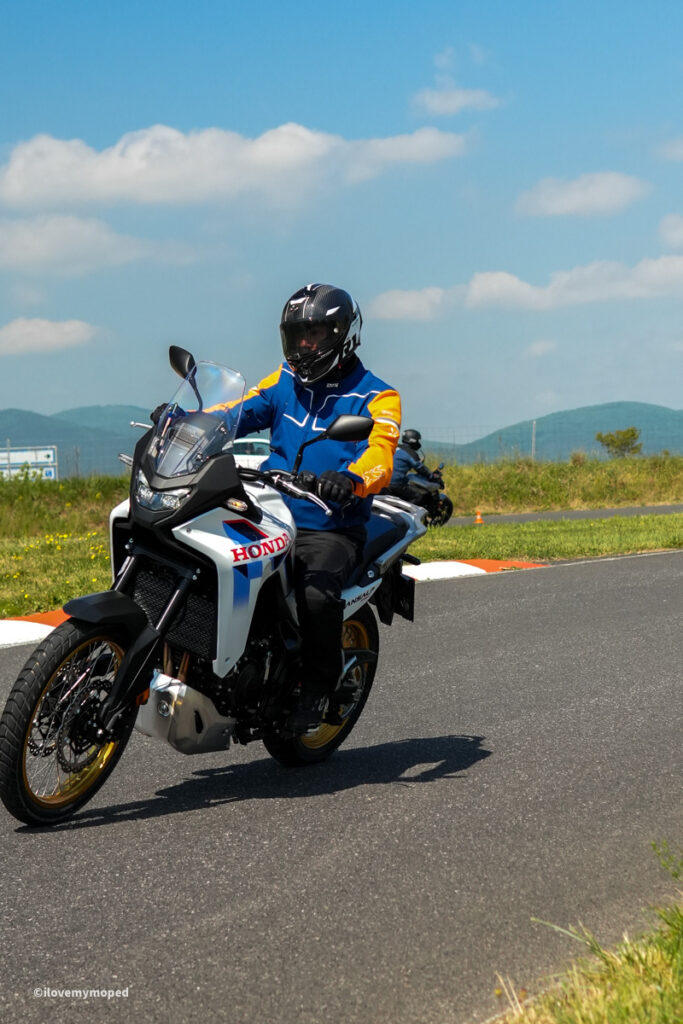 arge2rad-motorradtesttage2026-teesdorf-45 - I love my moped Motorcycle rider in a blue and orange jacket with full-face helmet on a Honda bike on a paved track with a blue sky.