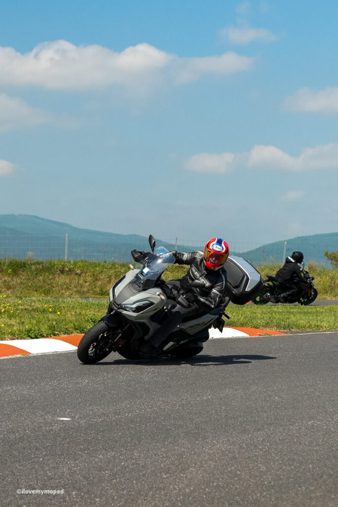 arge2rad-motorradtesttage2026-teesdorf-47 - I love my moped A motorcyclist wearing protective gear leans into a sharp turn on a race track, with another rider on a bike in the background under a blue sky.