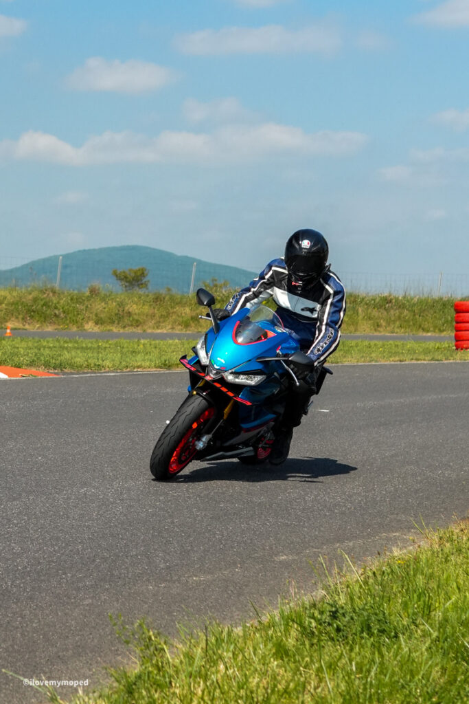 arge2rad-motorradtesttage2026-teesdorf-48 - I love my moped Motorcyclist in full gear leaning into a turn on a blue sport motorcycle on an outdoor race track with clear sky.