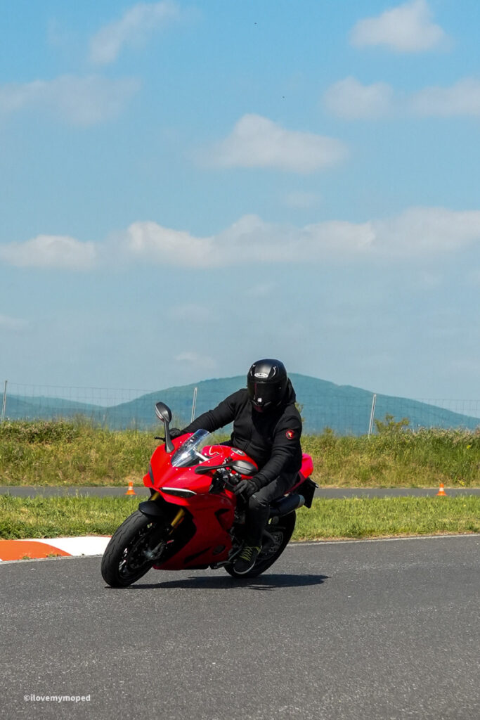 arge2rad-motorradtesttage2026-teesdorf-56 - I love my moped Rider in black protective gear leaning into a turn on a red sport motorcycle on a race track by a blue sky.