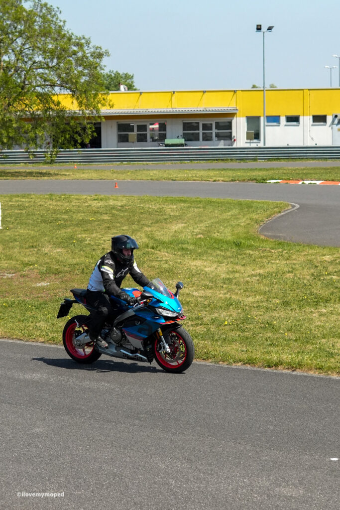 arge2rad-motorradtesttage2026-teesdorf-58 - I love my moped Motorcycle rider in helmet on a blue sportbike navigating a track curve with grassy infield and a yellow building in the background.