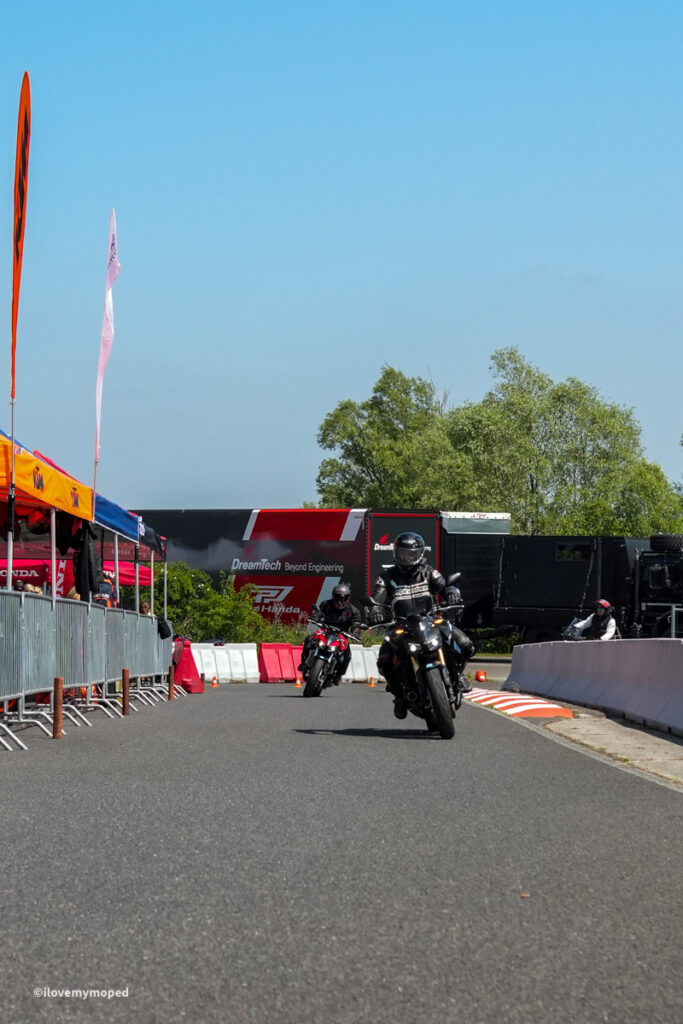 arge2rad-motorradtesttage2026-teesdorf-63 - I love my moped Motorcyclists riding on a closed road race course with barriers, tents, and banners on the side under a clear blue sky.