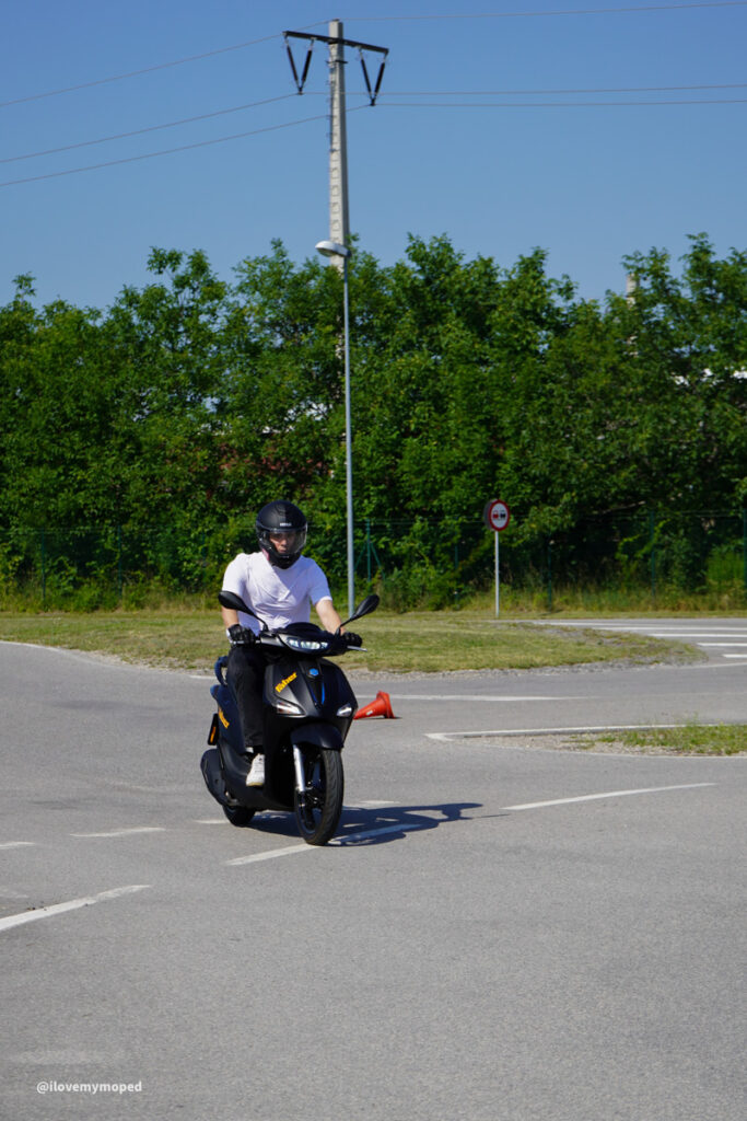 arge2rad-125ertesttag-arböfahrsicherheitszentrumwien-011 - I love my moped Motorcyclist wearing a helmet on a black scooter in an empty parking lot.