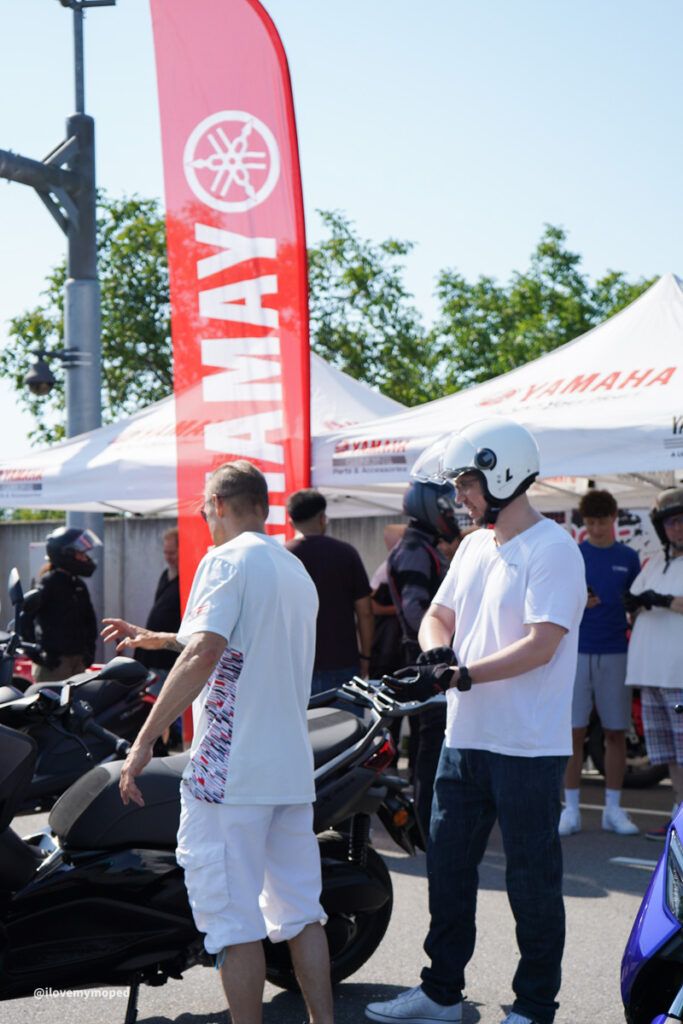 arge2rad-125ertesttag-arböfahrsicherheitszentrumwien-026 - I love my moped People at a Yamaha motorcycle event with riders and bikes under white tents and a tall red Yamaha banner in the background