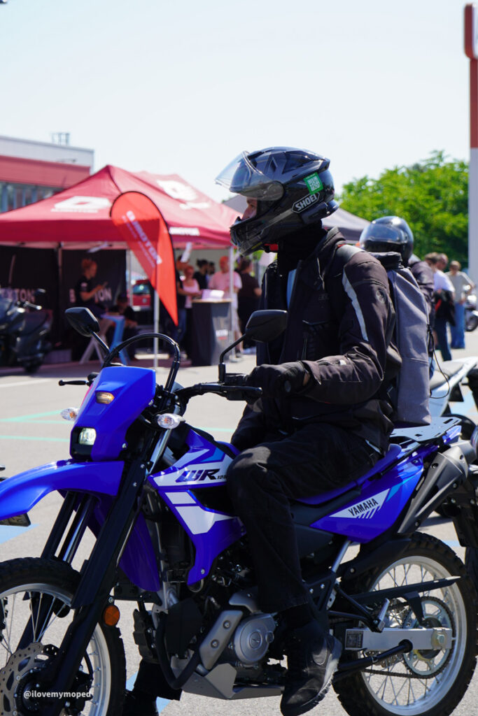 arge2rad-125ertesttag-arböfahrsicherheitszentrumwien-044 - I love my moped Motorcyclist wearing a full-face helmet and protective gear rides a blue Yamaha motorcycle at an outdoor event with red tents in the background.