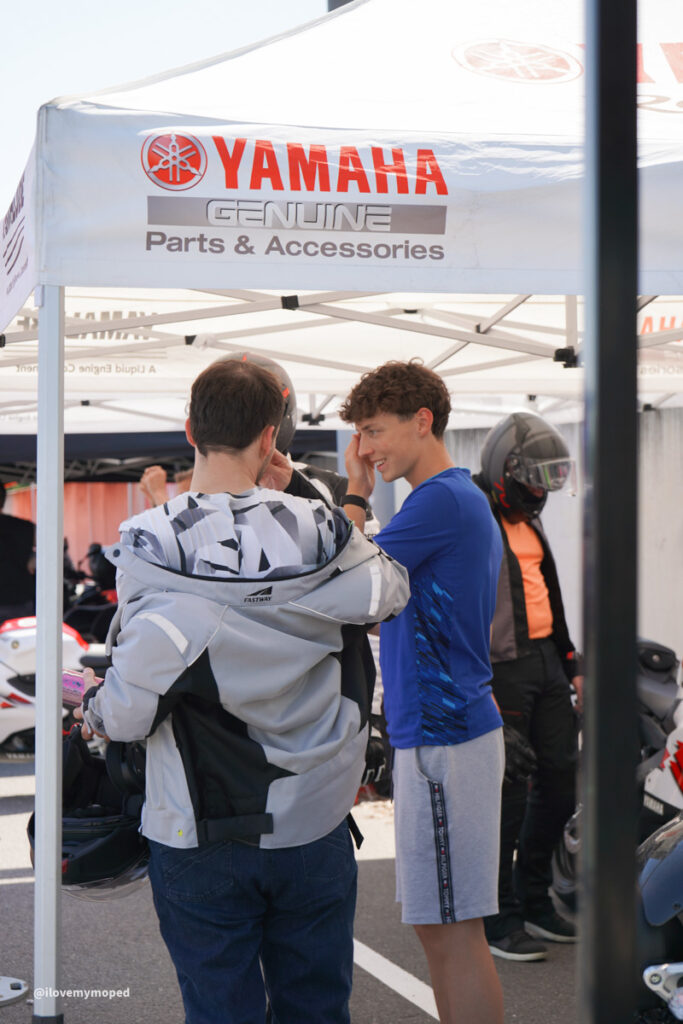 arge2rad-125ertesttag-arböfahrsicherheitszentrumwien-108 - I love my moped Two men under a Yamaha tent at a motorcycle event, one adjusting gear while the other talks nearby.