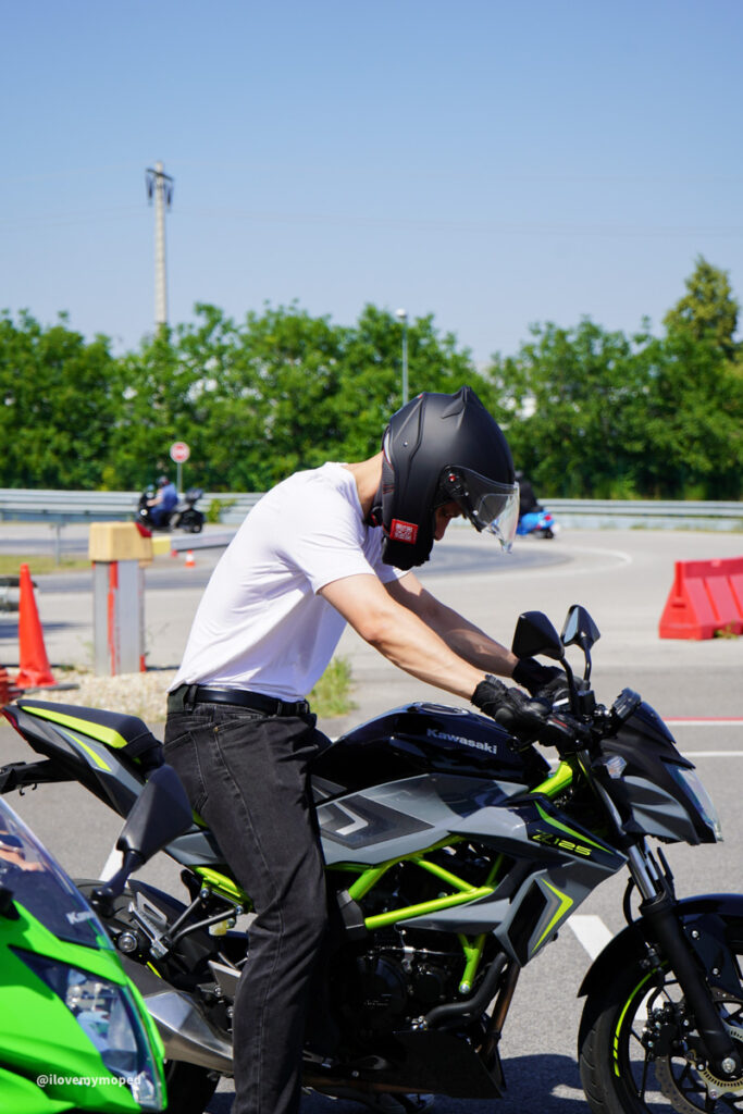 arge2rad-125ertesttag-arböfahrsicherheitszentrumwien-109 - I love my moped Rider wearing a black full-face helmet on a Kawasaki motorcycle with a neon-green frame, white shirt, and black jeans on a sunny track.